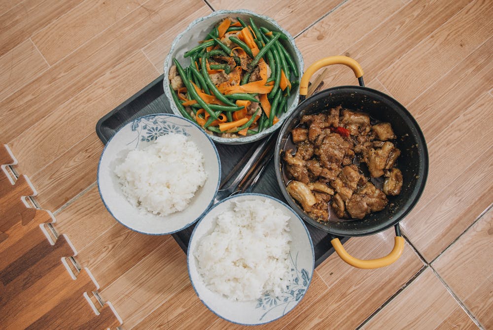 Close-up of a tasty Asian meal featuring pork, vegetables, and rice, beautifully arranged.