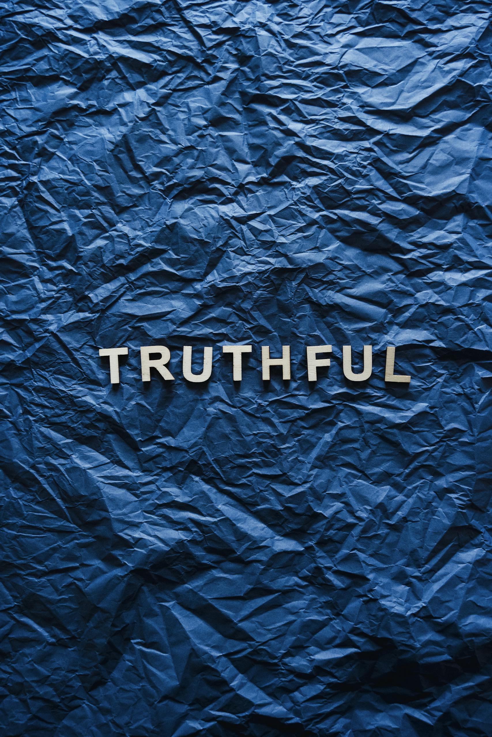 The word 'truthful' displayed on crumpled blue paper background.