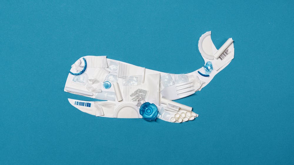 Eco-friendly concept art of a whale crafted from white plastic waste on a blue background.