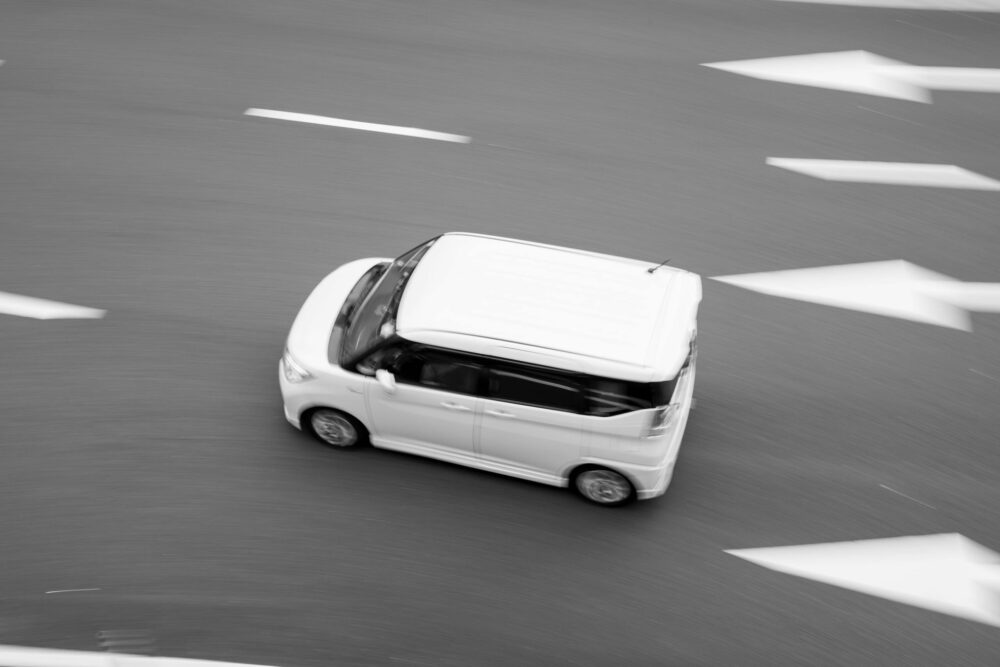 Black and white photo of a moving car on a road with directional arrows, emphasizing motion.