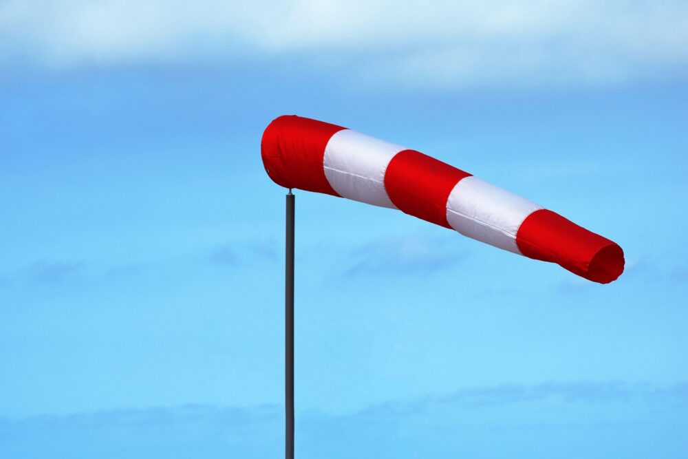 Red and white windsock indicating wind direction and speed against a clear blue sky.